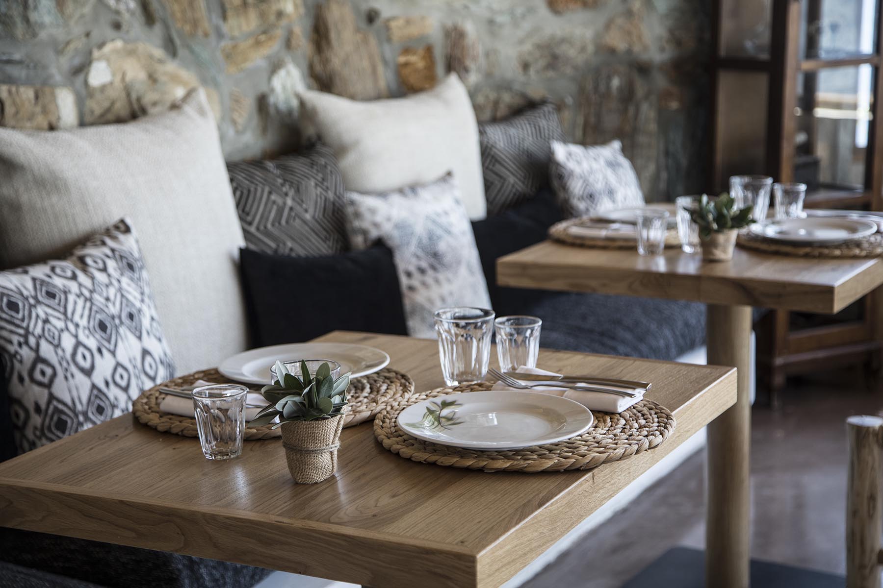The Minoan taverna at Seaside, rustic timber tables with woven placemats and cushions against a Cretan stone wall