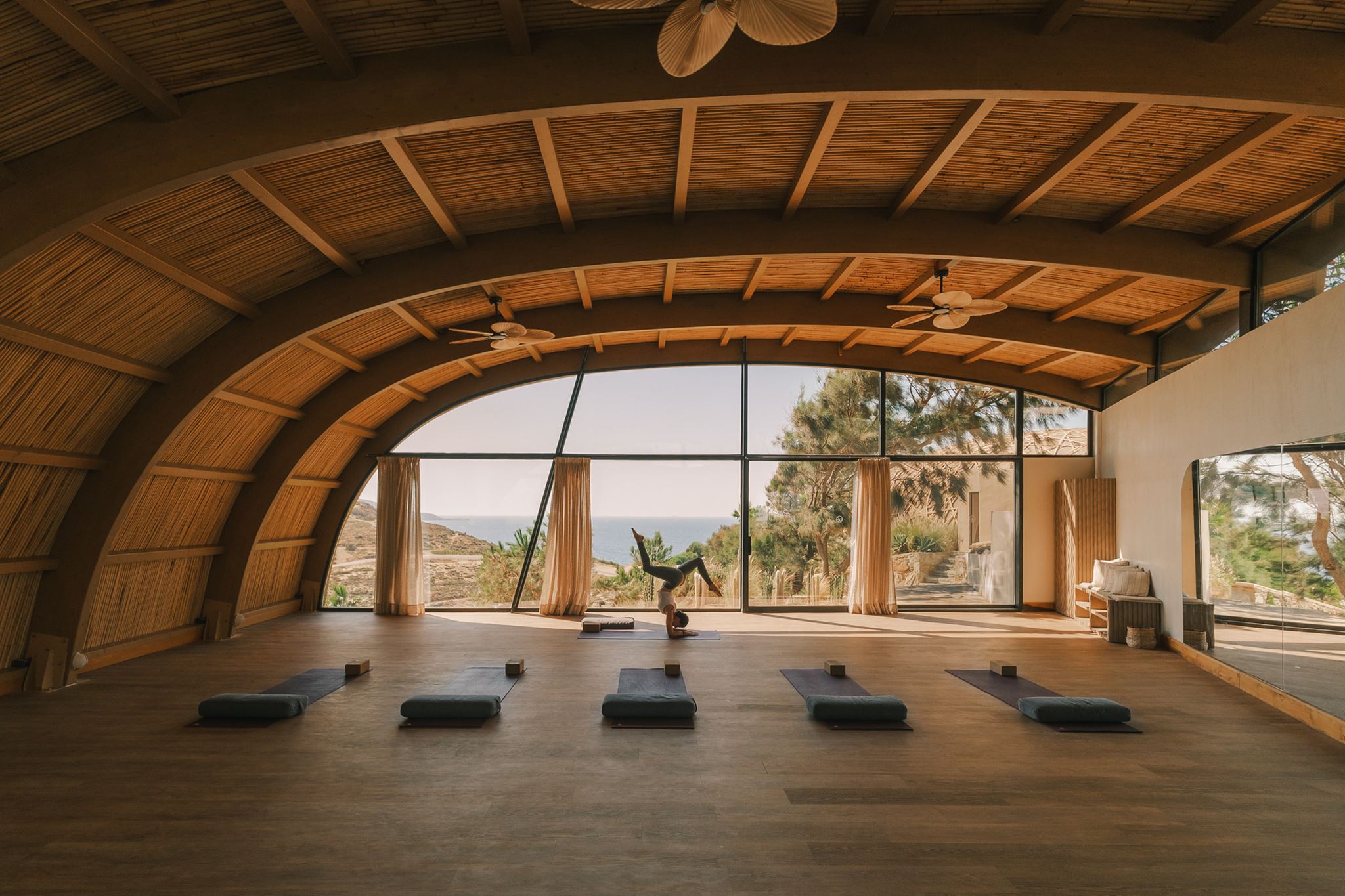 The bamboo vaulted ceiling of the Asana yoga shala at golden hour, mats laid out for practice