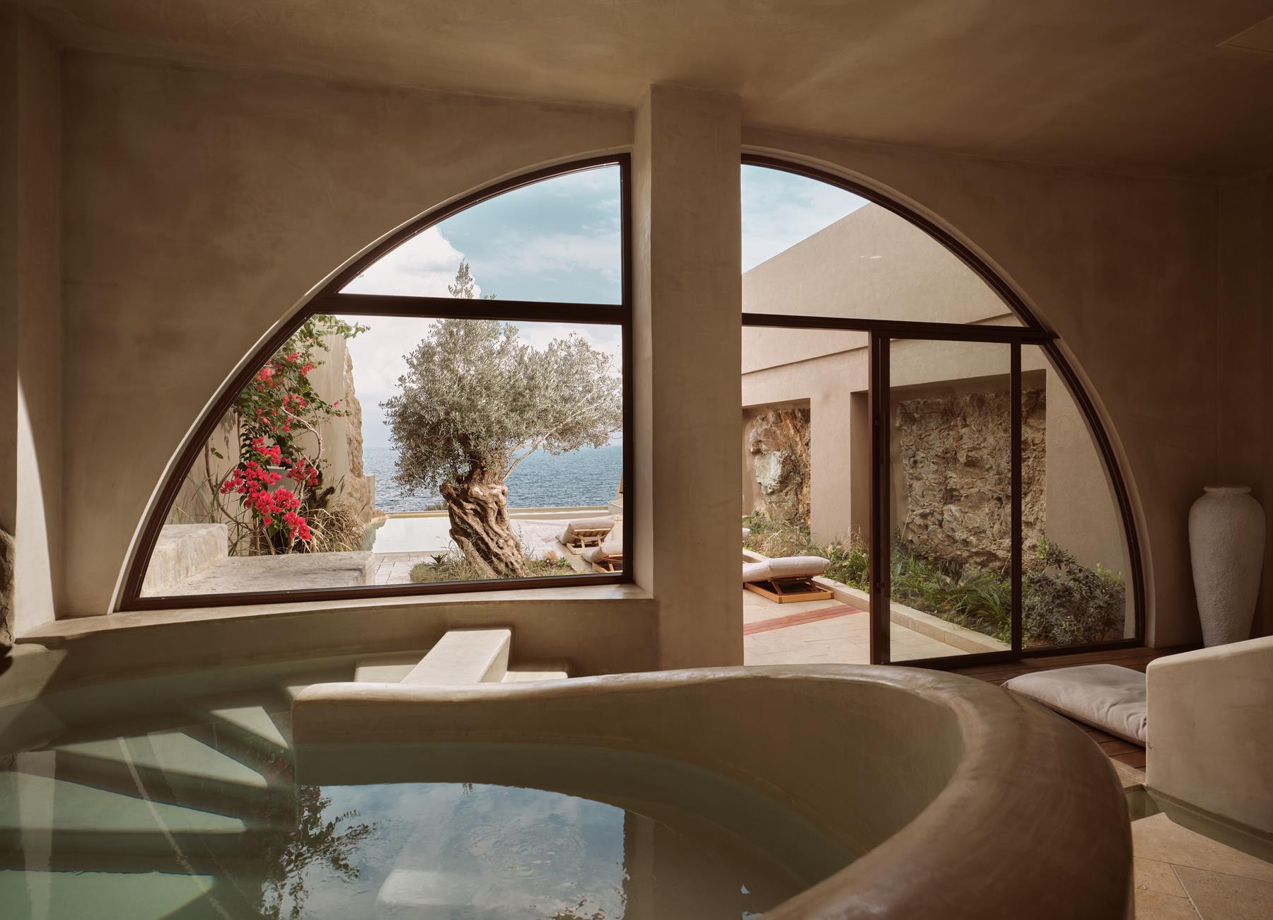 The Bathhouse pool framed by an arched window and olive tree courtyard